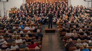 <p>Im Altarraum der evangelischen Kirche stehen 110 Sänger zweier Chöre. Die Kirchenbänke sind voll besetzt, die Veranstalter müssen noch Stühle bringen, damit alle Besucher sitzen können.</p>