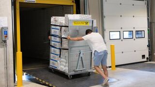 Ein Mitarbeiter schiebt eine versandfertige Ladung aus dem Logistikzentrum in den vorgefahrenen Lastwagen – Zeit ist im Versandhandel Geld.