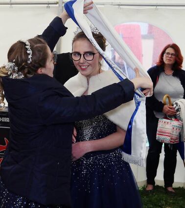 Janine hängt Anna die Schärpe um. Mama Manu-ela Schumacher schaut im Hintergrund zu.