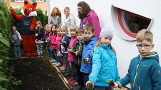 Konzentriert warten die Vorschulkinder darauf, dass sie die Blühbälle ins vorbereitete Beet werfen können. Auch Fred Fuchs hat eine Kugel aus Erde und Samen bekommen. In der hinteren Reihe schauen die Erzieherinnen Paula Becker (v. l.), Jacqueline Warschau und Kindergartenleiterin Simone Rey-Diehm dem Geschehen zu.