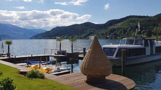 Im Garten von „KOLLERs“ Hotel: der Blick aus dem „Stone Cage“ am See, einer Sitzbank aus Holz, künstlerisch mit heimischen Bachsteinen ummantelt – ein „Lieblingsplatzerl“ der Gäste. Rechts ist das hoteleigene Relax-Schiff „MS KOLLERs Swan“ zu sehen, das neben dem Seebad vor Anker liegt.