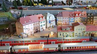 Die Züge halten in Bahnhöfen fantasievoll gestalteter Orte. Aus dem Speisewaggon des vorderen Zuges dringen sogar Stimmen: Es wird ein Salat geordert, Sektkorken knallen und der Küchenchef flucht.