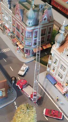 Die Straße ist gesperrt, es läuft ein Feuer-wehreinsatz. Die Drehleiter ist ausge-fahren, eine Laterne liegt am Boden.