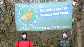 Das Banner der Bürgerinitiative „Rettet den Entenpfuhl“ haben Norbert Weiher (l.) und Heinz Eppel gut sichtbar am Waldrand aufgehängt.