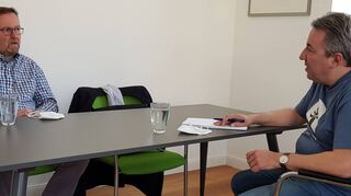 Der Schwetzinger Pfarrer und kommissarische Dekan Uwe Lüttinger im Gespräch mit Chefredakteur Jürgen Gruler in dessen gut durchlüftetem Büro. Da beide Abstand halten, haben sie für das Bild ihre FFP2-Masken abgenommen. Thema ist die Kirchenentwicklung 2030.