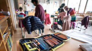 Ein Mäppchen liegt in einem Klassenraum auf einem Tisch. Für Grundschulen ist ab einer Inzidenz von unter 100 Präsenzunterricht in voller Gruppengröße möglich.