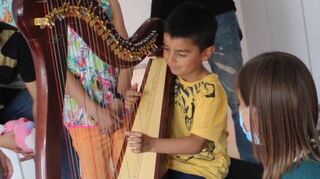 Mikail probiert zum ersten Mal im Leben die Harfe aus. Rachel Kelz (r.) zeigt ihm, wie er sie zum Klingen bringt.