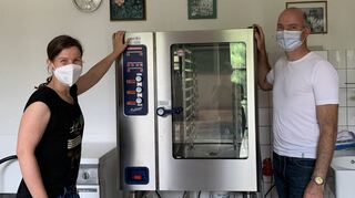 Pfarrerin Christiane Banse und Michael Ahnepohl vom Bauamt stehen im hinteren Raum der Küche neben einem Konvektomaten. In diesen kommt später das Essen für die Grundschulkinder.