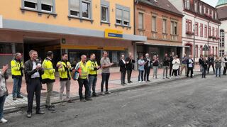 Applaus zur Eröffnung des ersten Bauabschnitts der Oberen Hauptstraße zwischen Fortunakreuzung/Heidelberger Straße (im Hintergrund) und Rathausstraße. Vertreter von Gemeinderat, Stadtverwaltung, Baufirma und Anwohnern freuen sich über die Information, dass der Zeit- und Kostenrahmen eingehalten wurde und auch die nächsten fertigen Teilbereiche gefeiert werden sollen, wie der OB verkündet.