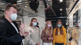 Dr. Torben-Schindler heißt Julia, Sinah und Sophie vom Gauß-Gymnasium in der Mitmachausstellung will-kommen und lädt sie ein, möglichst viel selbst auszuprobieren.
