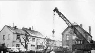Auf dem Bild des Gemeindearchivs ist der Abbau der Brückenwaage vor dem Feuerwehrhaus dokumentiert. Am linken Bildrand ist die Abdeckung des Tiefbrunnens erkennbar, im Hintergrund das Gasthaus „Zum Löwen“, die heutige Volksbank.