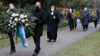 Fachbereichsleiterin Natascha Spahn und Oberbürgermeister Marcus Zeitler tragen gemeinsam einen Kranz über den Friedhof, dahinter folgen Pfarrer Johannes Heck sowie weitere Vertreter, die Kränze niederlegen.