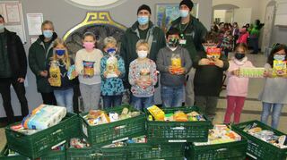 Schüler aus der Klasse 3a präsentieren stolz, was die Schule für Bedürftige gesammelt hat. Alexander, Nikolas, Angelika, Sascha und Sebastian (hinten v. l.) vom Tafelladen-Team haben beim Abtransport der vielen Kisten alle Hände voll zu tun.