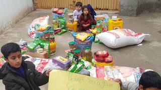 „Ein Dankeschön an Raquel und Schwetzingen“ steht auf dem gelben Schild, das die beiden afghanischen Jungen hochhalten. Im Hintergrund sind die Lebensmittel zu sehen, die mit Hilfe von Spenden aus der Kurpfalz gekauft werden konnten.