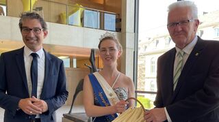 Schwetzingens Spargelkönigin Anna I. überreicht Ministerpräsidenten Winfried Kretschmann Schwetzinger Spargel. Der Grünen-Landtagsabgeordnete Dr. Andre Baumann (l.) aus Schwetzingen hat das hoheitliche Treffen eingefädelt.