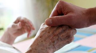 Ein Mitarbeiter eines Alten- und Pflegeheims hält die Hand einer Bewohnerin. Einen Menschen zum Lachen bringen, ihm Zeit zu schenken und ihm helfen zu können, könne die Seele füllen, sagen Marina Offenloch und Markus Hübl.