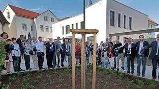 Symbolisch wird das Bäumchen im Hof von Gemeinderäten, Bürgermeistern, Politikern, Mitarbeitenden, dem Architektenteam und Mitgliedern des Jugendbeirates begossen – ein bedeutender Moment für alle Anwesenden.