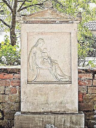 Das Grab von Mina auf dem Schwetzinger Friedhof. Der Grabstein ist aus weißem Marmor, inspiriert durch eine Griechenland-Reise mit ihrem Mann. Die Hinwendung zur Antike war damals typisch für die bildungsbürgerliche Schicht. Zu sehen ist eine Frau mit Kind, da Mina im Kindbett starb.
