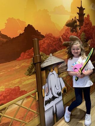 Leni ist bereit für das Ninjago-Abenteuer – sie lässt sich im neuen Ninjago-Quartier mit Meister Wu an der stimmungsvollen Landschaftstapete im Asia-Stil ablichten.