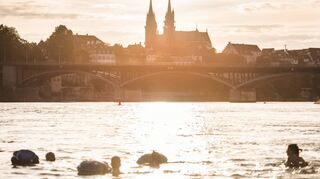 Panoramablick aufs Münster: Menschen treiben mit ihrem Wickelfisch in Basel den Rhein hinab.