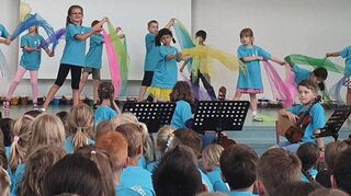 Die Erstklässler haben gemeinsam mit ihren Klassenlehrern einen farbenfrohen Tüchertanz einstudiert und beim Sommerfest präsentiert, die Zuschauer sind begeistert.