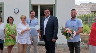 Bürgermeister Nils Drescher (3. v. r.) übergibt im Beisein von Gemeinderäten, Mitarbeitenden der Schulbetreuung Postillion und der Gemeinde den Schlüssel an Kernzeitleiterin Ilona Weiß.