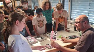 Christopher Tauber überreicht Autogrammkarten mit persönlicher Widmung. Der „Drei Fragezeichen“-Autor und -Illustrator bringt die Faszination der Kinderbuchserie in die Brühler Gemeindebücherei.