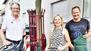 Bürgermeister Dr. Ralf Göck (v. l.), Silvia Klingel und Bauhofleiter Marcus Schütterle mit den neuen Brühler Baumpatengießkannen und den Wassersäcken vor einem der beiden Straßenbäume, die Silvia Klingel pflegt.