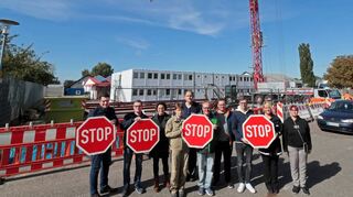 Bürgermeister Stefan Weisbrod (v. l.), Markus Kaletka, Bauamtsleiterin Ramona Drexler, Beate Zimmermann, Christian Antoni, Andreas Raab, Oliver Raab, Tobias Hardtmann (Bauamt), Beate Hecker (Ordnungsamt) und Diana Mehner signalisieren ihren Unmut mit Stopschildern. Im Hintergrund ist das Kranfahrzeug zu sehen, dass auf die weiteren Wohncontainer wartet, für deren Aufbau es noch keine Genehmigung gibt.