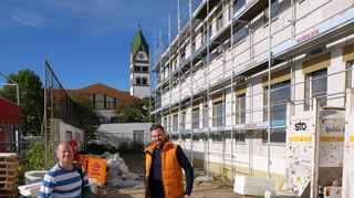 Architekt Tobias Maier (l.) und Bauamtsleiter Marc Schneider im künftigen „grünen Schulhof“ zwischen dem Anbau der Alten Schule (r.) und dem bunten Hort (l.). Während der Anbau der Alten Schule in Ketsch in großen Schritten vorankommt, sind nun auch die Planungen für das Außengelände Richtung Schwetzinger Straße beschlossen: Hier entsteht ein grüner Pausenhof samt kleinem Fußballplatz.