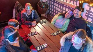 Zwei Hockenheimerinnen probieren das Dinner in the Dark: Lea Jung (links vorne) und ihre Cousine Laurine Müller (rechts daneben) setzen ebenso wie Paula und Tina Schäfer (l.) sowie Annette und Martin Karaus (2. und 3. v. r.) beim Essen Masken auf.