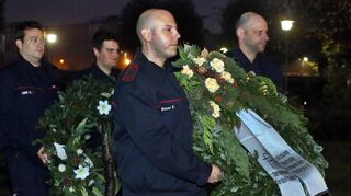 Die Feuerwehrkameraden tragen die Gedenkkränze über den Friedhof.