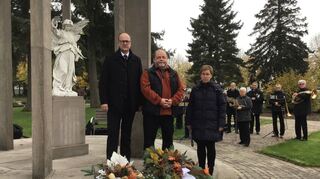 Bürgermeister Gunther Hoffmann (v.l.), Bodo Häusler (VdK) und Pfarrerin Katharina Garben am Friedensengel auf dem Friedhof. Im Hintergrund der Musikverein.