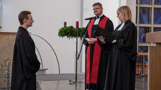Simon Layer (l.) vernimmt die Worte der Berufungsurkunde durch Christine Wolf, noch ehe Pfarrer Tobias Habicht (M.) die Segnung übernimmt.