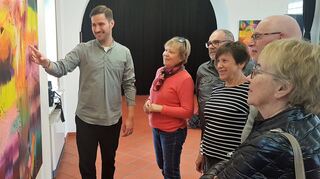 Maximilian Löffler erläutert den Besuchern im Alten Bahnhof seine teils überaus strahlenden Bilder.