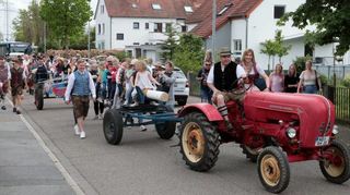Ein kleiner Festzug durch die Rheintalstraße bringt den Maibaum zu seinem Aufstellungsort. Vorne fährt Robert Heinrich den Oldtimer-Traktor.