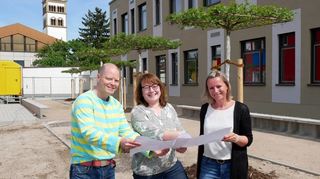 Architekt Tobias Maier sowie Petra Brandenburger (M.) und Melanie Dosch vom Bauamt der Gemeinde vor dem frisch gepflanzten Blätterdach im neuen Schulhof.