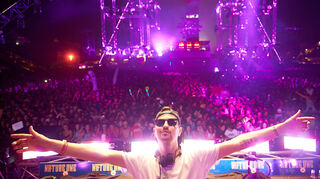 DJ Robin Schulz steht 2016 beim Technofestival "Nature One" mit ausgestreckten vor einem DJ-Pult.