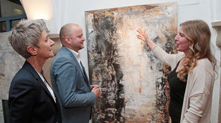 Künstlerin Alexandra Ulrich (r.) stellt derzeit im Gewölberaum in der Eichendorffstraße 2 aus. Während der Vernissage stellt sie Organisatorin Ute Walter von der Gemeinde und Bürgermeister Pascal Seidel das Bild „Phönix“ vor.