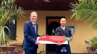 Bürgermeister Dr. Ralf Göck (l.) ist sichtlich beeindruckt von der großen Peperonitorte, die Wirt Flavio Assenza zur Eröffnung der neu gestalteten Terrasse des „Ristorante Peperoncino“ unter Palmen präsentiert.