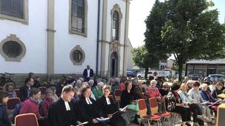 Die Seelsorger Johannes Heck (v. l.), Eva Weisser und Katharina Garben sitzen beim Gottesdienst unter freiem Himmel im Schatten der evangelischen Kirche in der ersten Reihe.