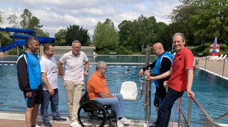 Der kommunale Behindertenbeauftragte Rudi Bamberger (Mitte) und Bäderchef Patrik Berndt (2. v. r.) fachsimpeln im Beisein (v. l.) von Schwimmmeister Marc Herbel, den Rathausmitarbeitern Kai Rill und Dirk Faulhaber sowie Bürgermeister Dr. Ralf Göck über den neuen Poollift im Freibad.
