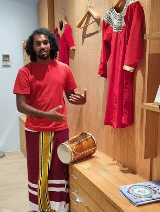 Sultan vom Maldives Discovery Centre auf Crossroads trägt die traditionelle Kleidung für Männer (Feyli). An der Wand ist das Gewand für Frauen zu sehen.