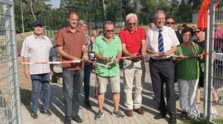 Bürgermeister Dr. Ralf Göck (Mitte) durchschneidet umringt von Ratsmitgliedern zusammen mit (am Band v. l.) Christof Diehl vom Bauunternehmen, Jugendleiter Horst Wiesner und dem SVR-Vorsitzenden Hans Hufnagel zur offiziellen Freigabe des Platzes das Absperrband.