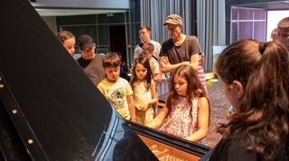 Mit Klavierbauer Markus Rau (M.) wagen die Teilnehmer eines Workshops einen Blick ins Innere des Instrumentes. Die Funktions-weise wird dadurch eindrucksvoll sichtbar.