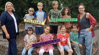 Für unsere Zeitung kehren Leo (hinten v. l.), Simon, Linus, Lino, Talin (vorne v. l.), Paulina, Luzia und Theo noch einmal an den Drehort zurück. In den Händen halten sie die im Video-Clip verwendeten Schilder. Rektorin Annett Mellentin (l.) und Annabell Heck vom Freundeskreis sind stolz auf die jungen Preisträger des Vereins Kommunale Kriminalprävention.