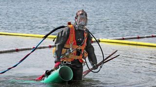 Taucher Alexander Kesberg kommt mit dem Sauger, dem „Injektor“ (grün), aus dem Wasser.