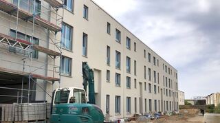 Haus B ist sogar schon fertig verputzt – das Gerüst ist abgebaut. Links ist die Tiefgarageneinfahrt zu sehen, die über die Pfaudlerstraße zu erreichen ist.