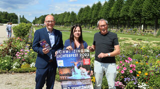 Schwetzingens Oberbürgermeister Dr. René Pöltl, Tatjana Lorenz von der Schlossverwaltung und „Yellow Concert“-Vertreter Erwin Clausen präsentieren das Ankündigungs-plakat für das Lichterfest am 29. Juli im Schlossgarten.