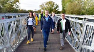 <p>Ende Oktober 2022 erfolgte die Freigabe der Ahrmündungsbrücke - eine enorm wichtige Brücke für Sinzig und das Ahrtal. Vorneweg schreitet Sinzigs Bürgermeister Andreas Geron mit weiteren Offiziellen.</p>
<p>Das im Naturschutzgebiet liegende Bauwerk stellt eine wichtige Verbindung für den kleinräumigen Fußgänger- und Radfahrverkehr zwischen Sinzig und Remagen dar – gerade auch für Pendlerinnen und Pendler. Zudem ist die Brücke Teil eines Radweges mit einer weit überregionalen Bedeutung: Als Rheinradweg und Eurovelo-Route 15 gehört er zu den wichtigsten Radfernwegen Europas und verbindet auf etwa 1200 km das schweizerische Andermatt in den Alpen mit dem niederländischen Hoek van Holland an der Nordsee.</p>
